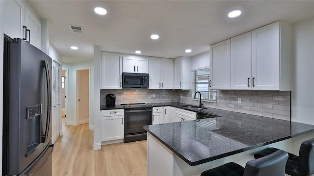 2970 Lantern Dr, South Daytona, FL 32119 - kitchen with black appliances, a peninsula, light wood-style floors, a breakfast bar area, and white cabinets