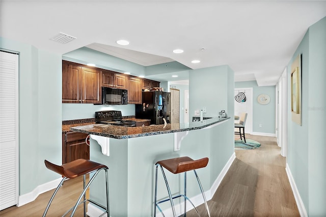 3315 S Atlantic Ave Unit 1605, Daytona Beach Shores, FL 32118 - kitchen featuring black appliances, a kitchen breakfast bar, light wood-type flooring, dark stone counters, and recessed lighting