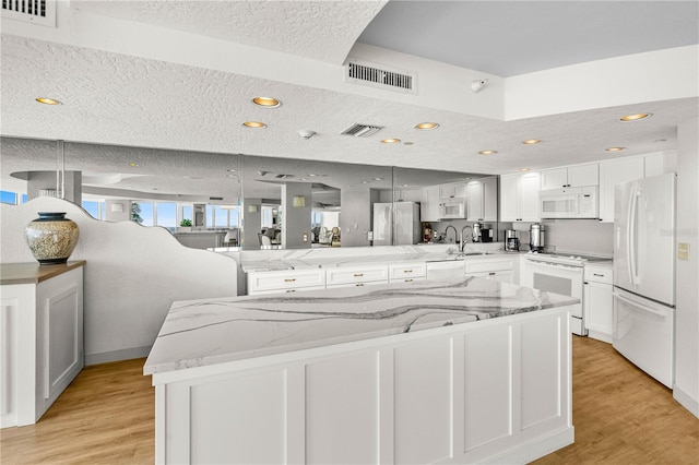 2545 S Atlantic Ave Unit 102, Daytona Beach Shores, FL 32118 - kitchen featuring white appliances, a peninsula, light wood-type flooring, light stone counters, and a textured ceiling