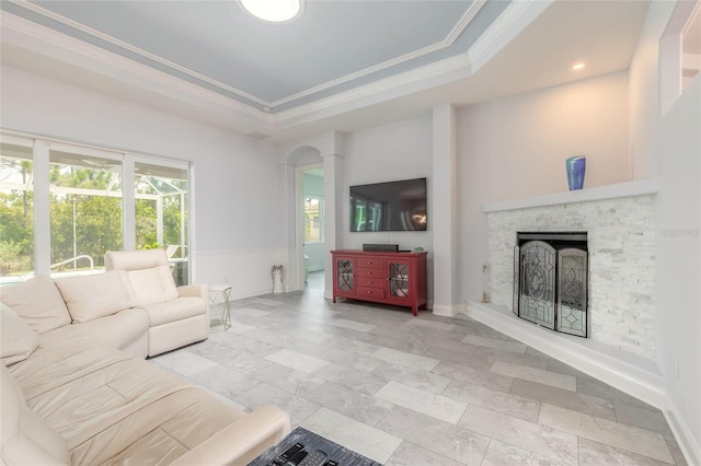2816 E Venetian Lake Cir, New Smyrna Beach, FL 32168 - living room featuring a raised ceiling, a stone fireplace, ornamental molding, wainscoting, and arched walkways