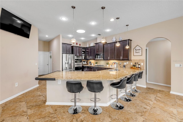 710 Grape Ivy Ln, New Smyrna Beach, FL 32168 - kitchen with appliances with stainless steel finishes, light stone counters, a peninsula, arched walkways, and a breakfast bar