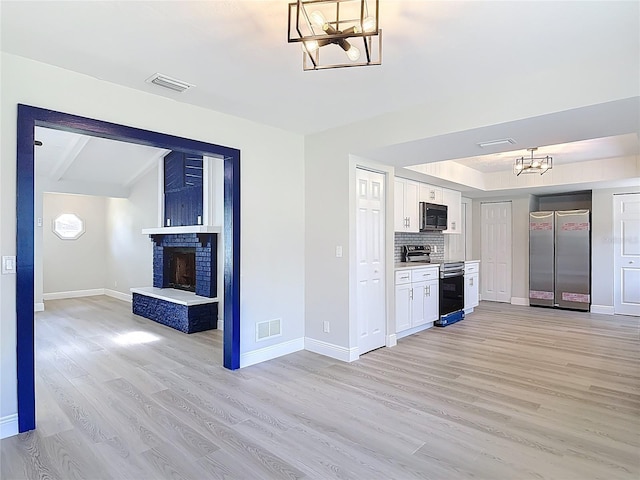 1019 Chippewa Trl, Daytona Beach, FL 32117 - kitchen with stainless steel appliances, a chandelier, light wood-style flooring, white cabinets, and a brick fireplace