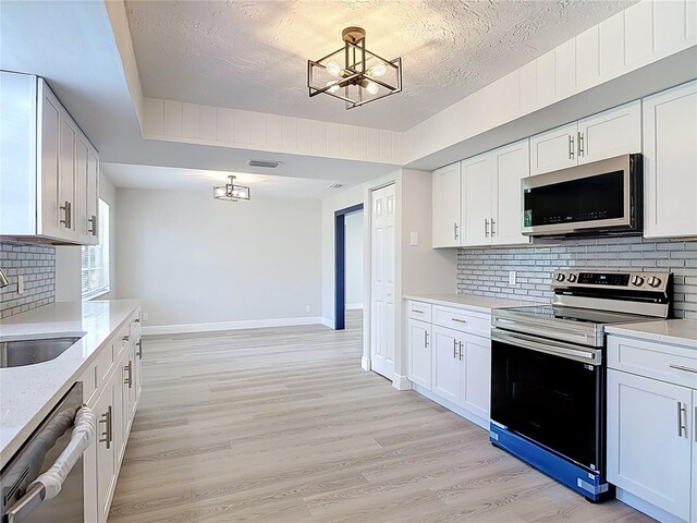 1019 Chippewa Trl, Daytona Beach, FL 32117 - kitchen featuring stainless steel appliances, a chandelier, decorative backsplash, light wood-type flooring, and white cabinetry