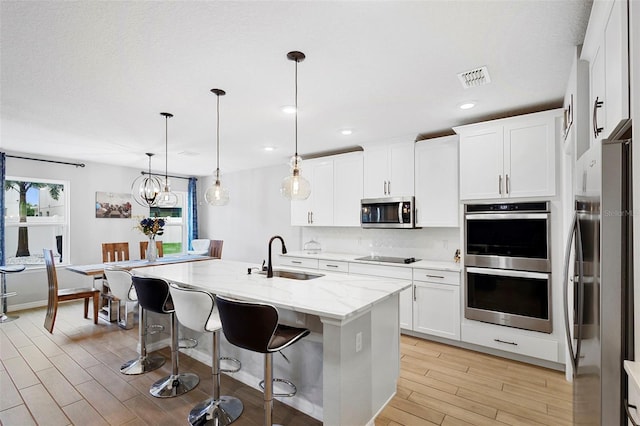 2807 Priego Blvd, Kissimmee, FL 34744 - kitchen featuring stainless steel appliances, light wood-style floors, backsplash, light stone countertops, and an island with sink