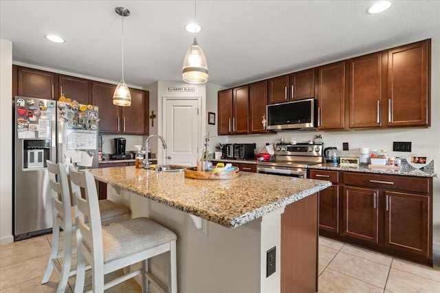 815 Fillmore Ct, Davenport, FL 33837 - kitchen featuring appliances with stainless steel finishes, light tile patterned floors, light stone counters, an island with sink, and a kitchen bar