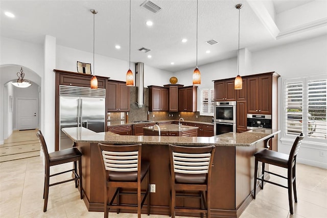 12812 Jacob Grace Ct, Windermere, FL 34786 - kitchen featuring stainless steel appliances, a large island with sink, backsplash, arched walkways, and light tile patterned floors
