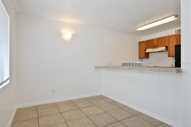 415 N Halifax Ave Unit 109, Daytona Beach, FL 32118 - kitchen featuring under cabinet range hood, light countertops, light tile patterned floors, brown cabinets, and freestanding refrigerator