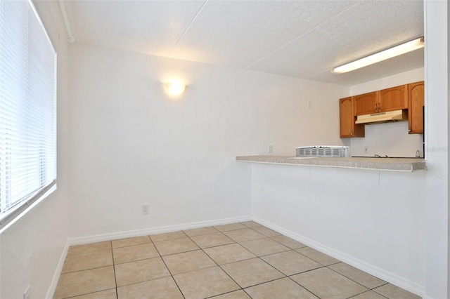 415 N Halifax Ave Unit 109, Daytona Beach, FL 32118 - kitchen featuring under cabinet range hood, light countertops, light tile patterned flooring, brown cabinetry, and a textured ceiling