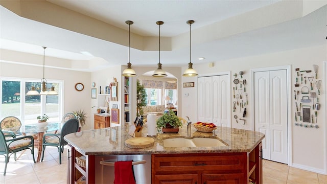 kitchen with a tray ceiling, a kitchen island with sink, sink, and decorative light fixtures