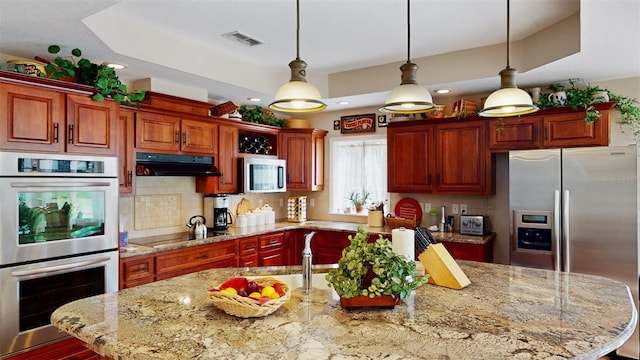 kitchen featuring tasteful backsplash, a center island, pendant lighting, stainless steel appliances, and light stone countertops