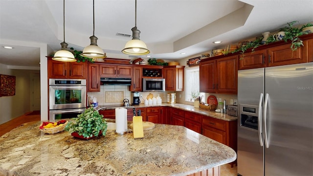 kitchen featuring pendant lighting, light stone counters, stainless steel appliances, and a kitchen island