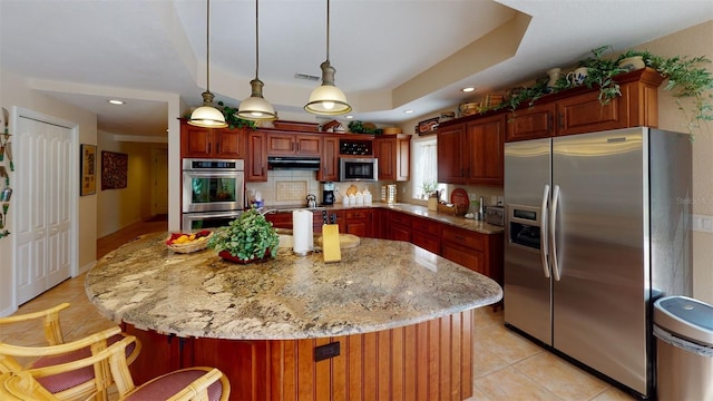 kitchen featuring light stone counters, stainless steel appliances, hanging light fixtures, and a kitchen island