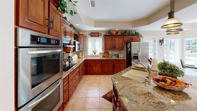 kitchen featuring sink, light stone counters, a tray ceiling, pendant lighting, and stainless steel appliances