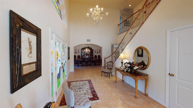 hall featuring light tile patterned flooring, a towering ceiling, an inviting chandelier, and french doors