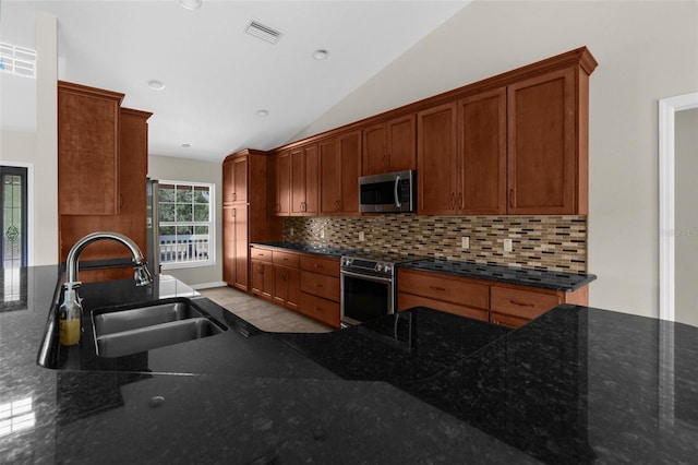 kitchen with lofted ceiling, sink, appliances with stainless steel finishes, backsplash, and dark stone counters