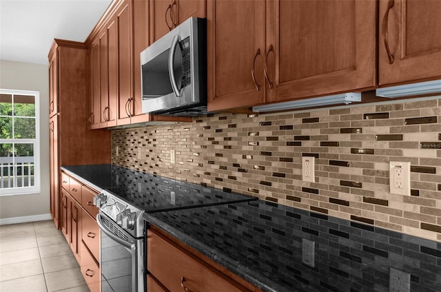 kitchen with dark stone countertops, backsplash, light tile patterned floors, and stainless steel appliances