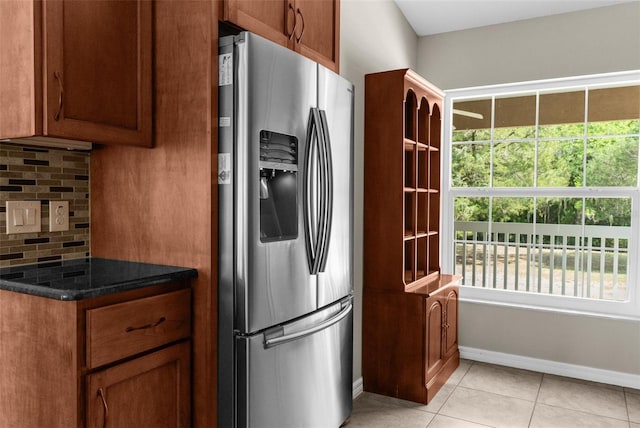 kitchen with stainless steel refrigerator with ice dispenser, light tile patterned floors, tasteful backsplash, and dark stone countertops