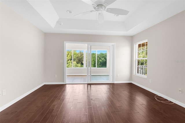 unfurnished room featuring a raised ceiling, dark wood-type flooring, and ceiling fan