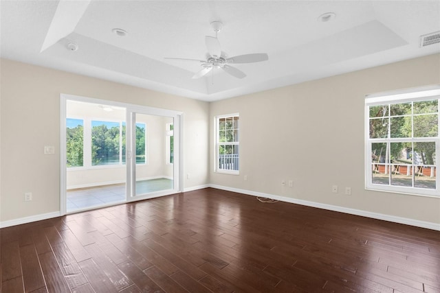 empty room with dark wood-type flooring, a wealth of natural light, ceiling fan, and a tray ceiling