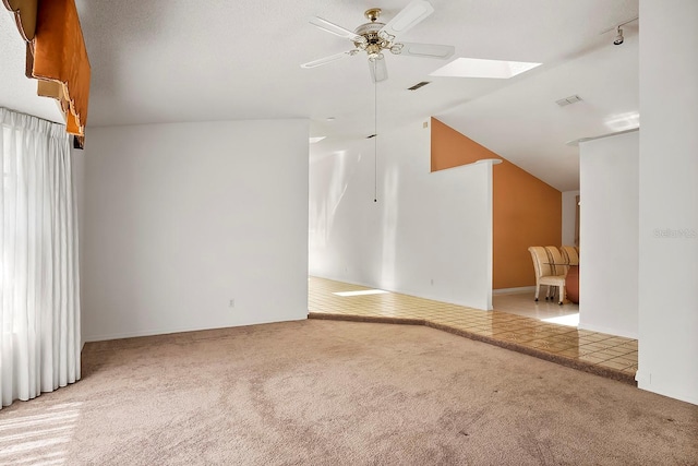 carpeted spare room featuring vaulted ceiling with skylight and ceiling fan