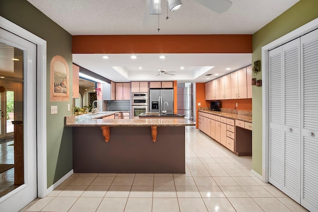 kitchen with light stone countertops, ceiling fan, kitchen peninsula, appliances with stainless steel finishes, and a raised ceiling