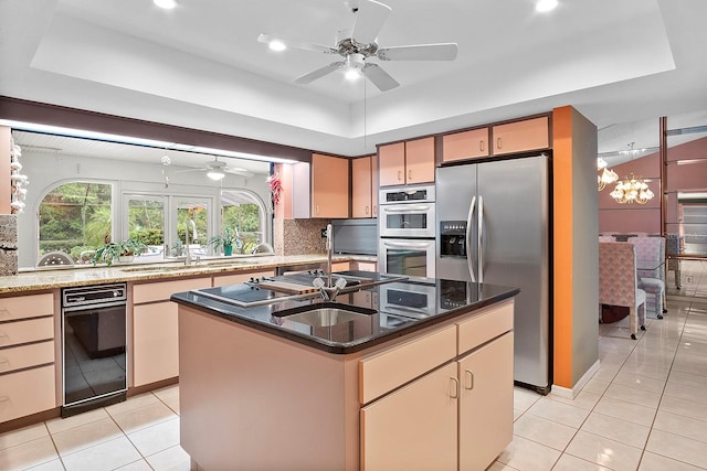 kitchen featuring light tile floors, appliances with stainless steel finishes, backsplash, a center island with sink, and ceiling fan with notable chandelier