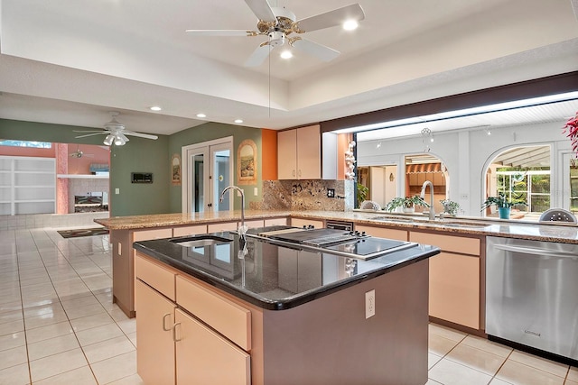 kitchen with ceiling fan, a center island with sink, stainless steel dishwasher, a tile fireplace, and tasteful backsplash