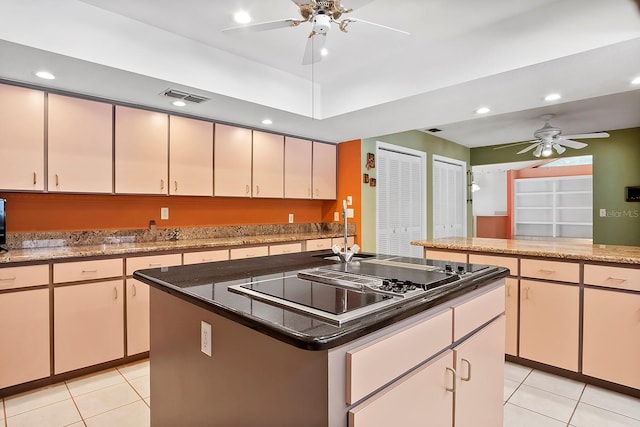 kitchen with ceiling fan, black electric cooktop, light tile floors, a center island, and dark stone countertops