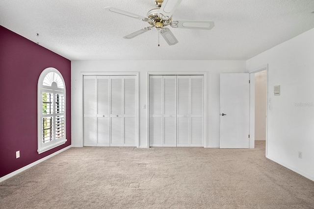 unfurnished bedroom with light carpet, a textured ceiling, ceiling fan, and two closets