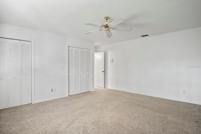 unfurnished bedroom featuring light carpet, multiple closets, a textured ceiling, and ceiling fan