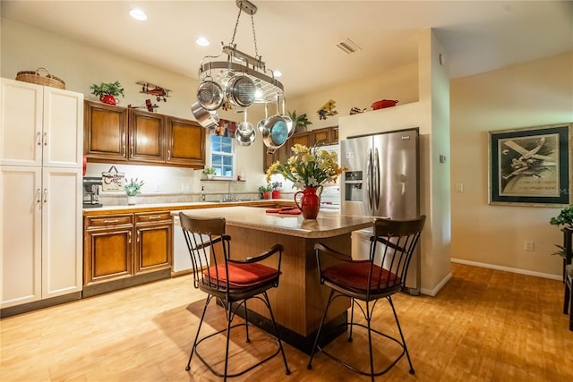 kitchen featuring a center island, sink, light hardwood / wood-style floors, stainless steel fridge with ice dispenser, and a breakfast bar area