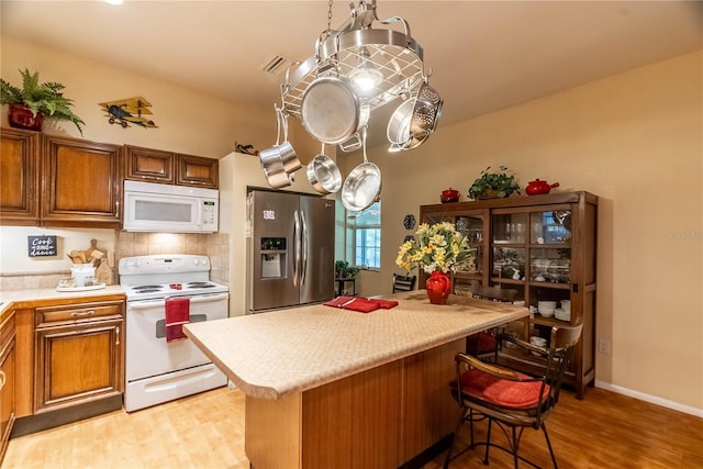 kitchen featuring light wood-type flooring, backsplash, white appliances, decorative light fixtures, and a breakfast bar area