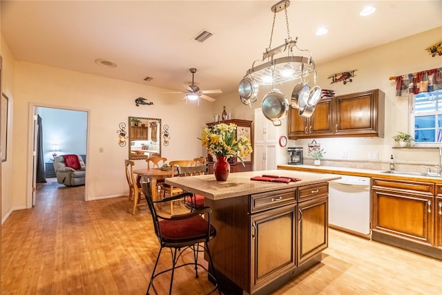 kitchen featuring dishwasher, sink, ceiling fan, a kitchen island, and a kitchen bar