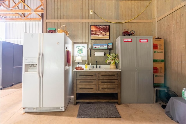 kitchen with white refrigerator with ice dispenser, sink, concrete floors, and wood walls