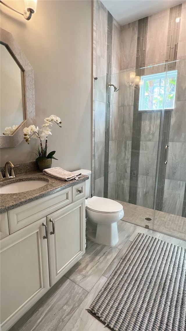 bathroom with toilet, a shower with shower door, and vanity