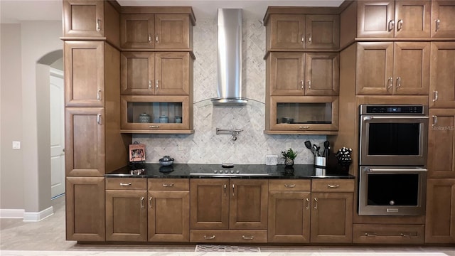 kitchen featuring light tile floors, stainless steel double oven, dark stone countertops, black electric cooktop, and wall chimney exhaust hood