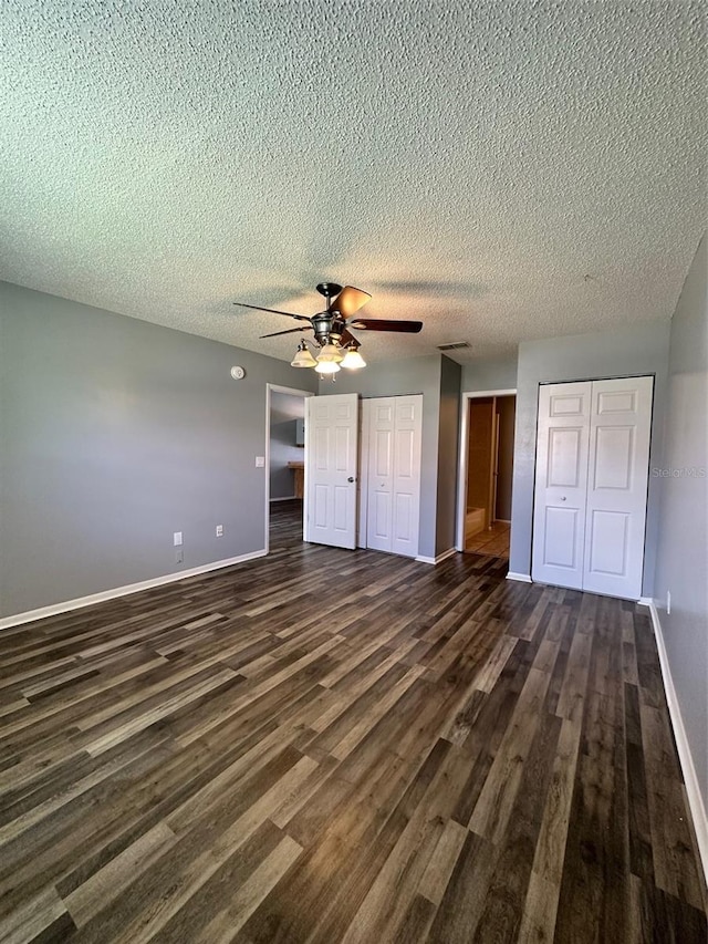 unfurnished bedroom featuring a textured ceiling, multiple closets, ceiling fan, and dark hardwood / wood-style floors