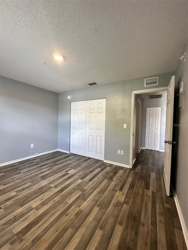 unfurnished bedroom featuring a textured ceiling, a closet, and dark wood-type flooring