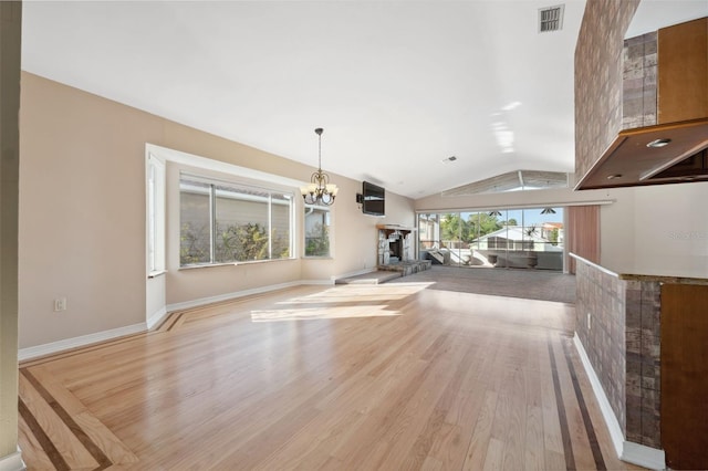 kitchen with lofted ceiling, a fireplace, an inviting chandelier, light hardwood / wood-style floors, and pendant lighting