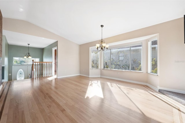 spare room featuring an inviting chandelier, vaulted ceiling, and light wood-type flooring