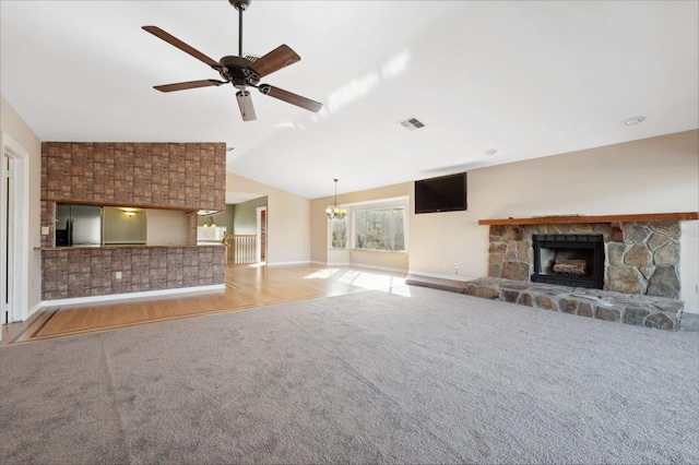 unfurnished living room with light carpet, vaulted ceiling, a stone fireplace, and ceiling fan with notable chandelier