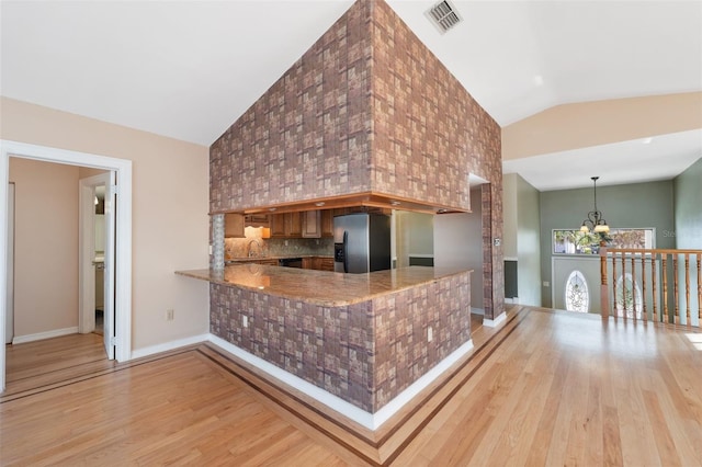 kitchen featuring kitchen peninsula, stainless steel fridge with ice dispenser, a chandelier, light hardwood / wood-style floors, and high vaulted ceiling