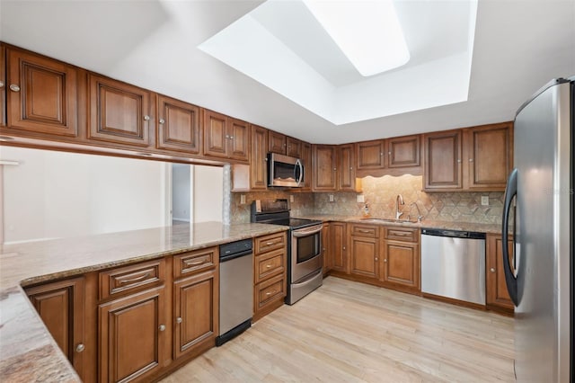 kitchen featuring light hardwood / wood-style floors, stainless steel appliances, tasteful backsplash, and light stone counters