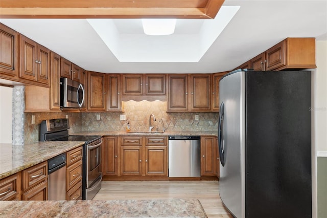 kitchen with sink, backsplash, light hardwood / wood-style floors, stainless steel appliances, and light stone countertops