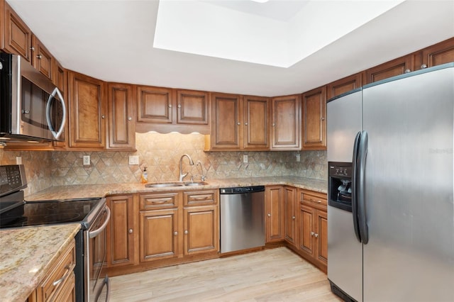 kitchen with light stone countertops, appliances with stainless steel finishes, sink, light hardwood / wood-style flooring, and tasteful backsplash