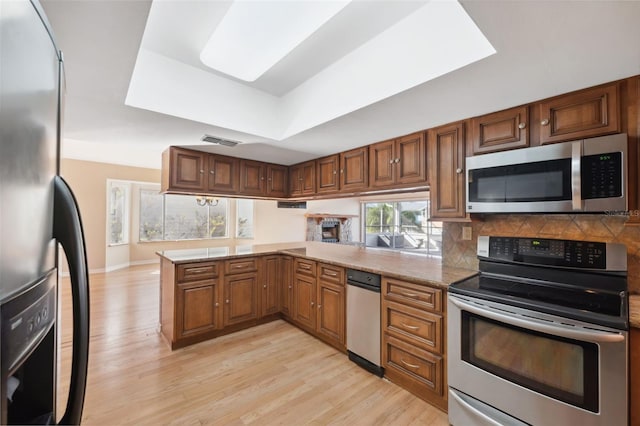 kitchen with kitchen peninsula, light stone countertops, light wood-type flooring, stainless steel appliances, and a raised ceiling