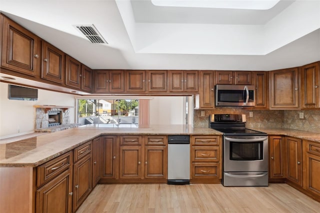 kitchen with appliances with stainless steel finishes, light hardwood / wood-style flooring, a tray ceiling, light stone countertops, and tasteful backsplash