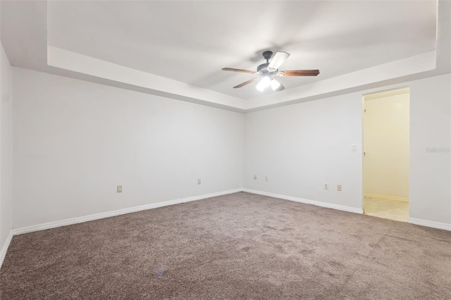 spare room with a raised ceiling, ceiling fan, and light colored carpet