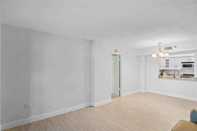 unfurnished living room with sink, light hardwood / wood-style floors, and a chandelier