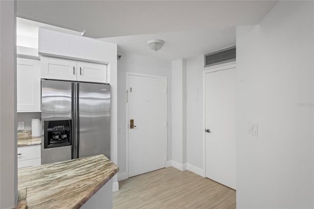 kitchen with light wood-type flooring, stainless steel fridge with ice dispenser, and white cabinets